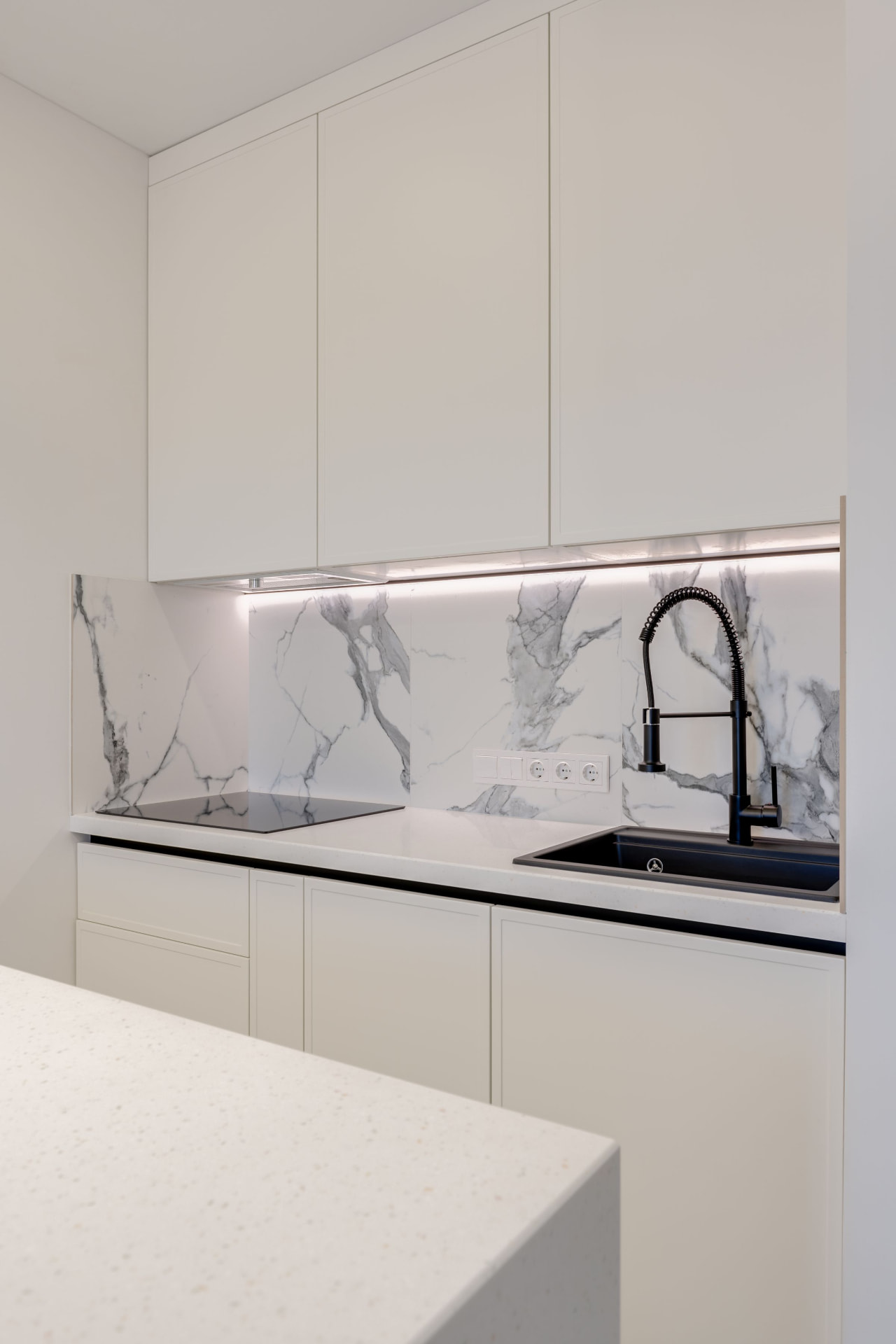 Handleless white frameless cabinets with a marble backsplash and black fixtures