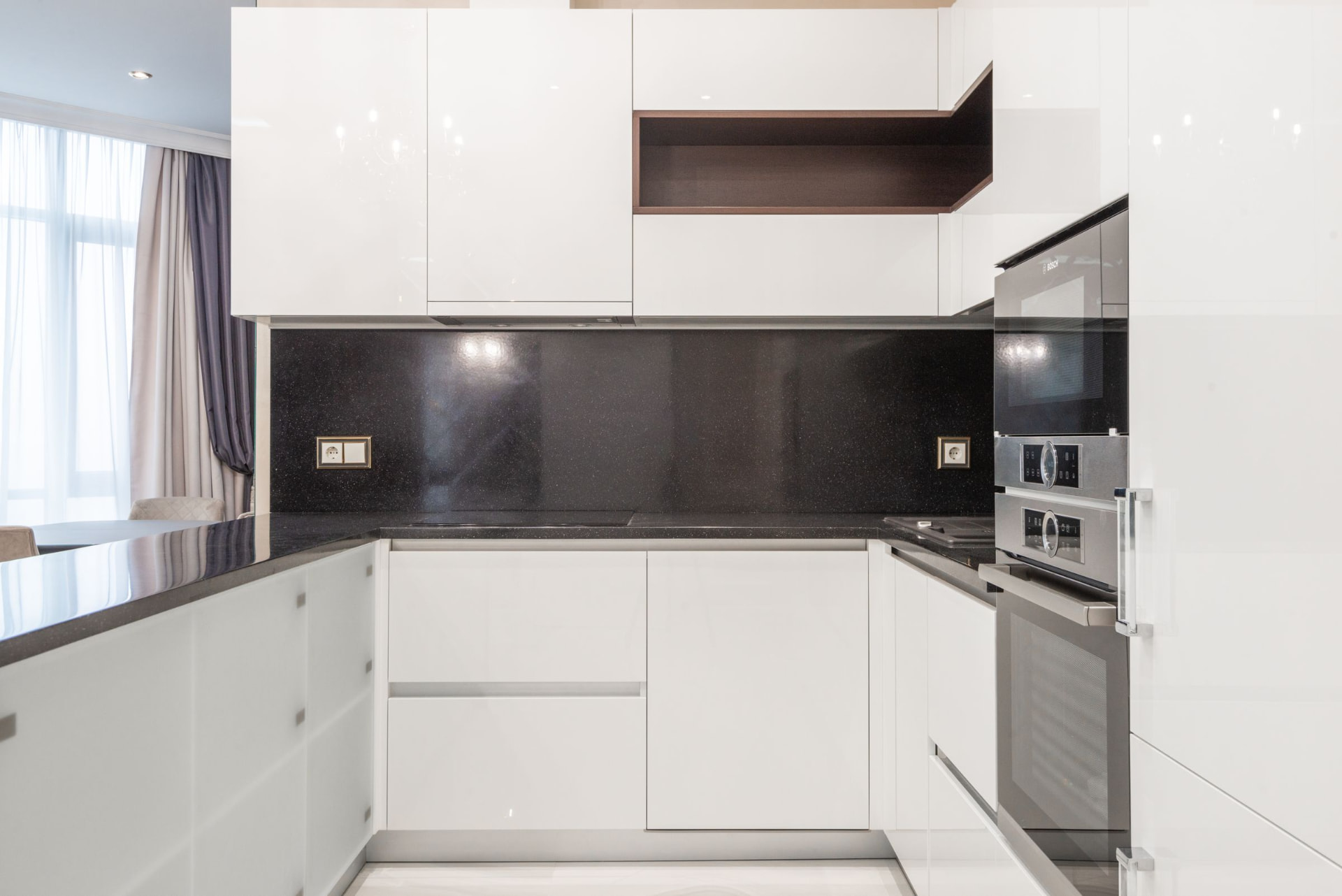 High-gloss white kitchen with a black stone backsplash and built-in ovens
